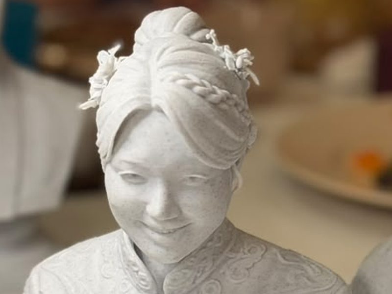 Close-up of a marble statue caricature showing braided hair and embroidered collar
